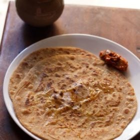 aloo gobi paratha on white plate with pickle by the side.