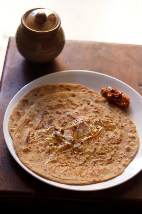 aloo gobi paratha on white plate with pickle by the side.