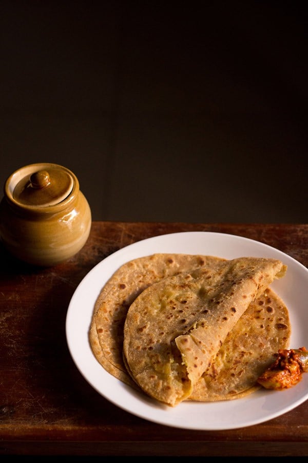 aloo gobi paratha served with pickle on a white plate. 