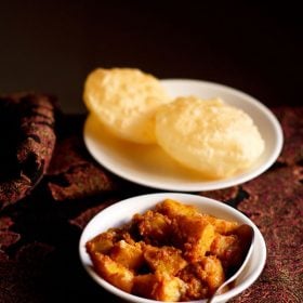 alur dom served in a white bowl with a spoon inside it and luchi on a white plate.