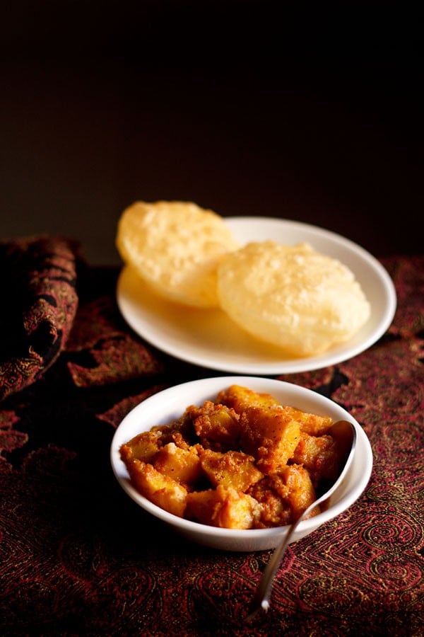 alur dom served in a white bowl with a spoon inside it and luchi on a white plate.