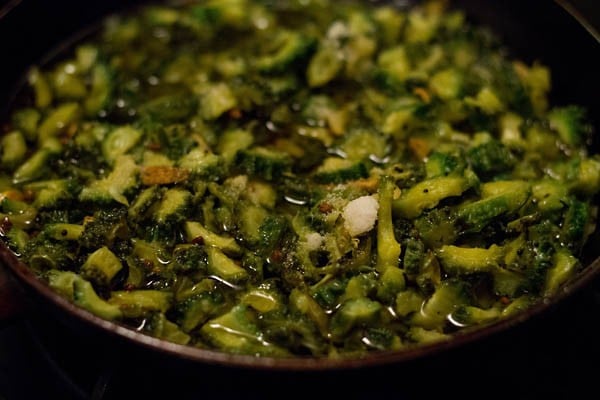 adding white vinegar and salt to the bitter gourd pieces in the hot oil. 