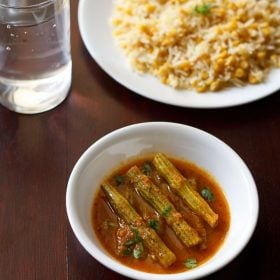 drumstick curry garnished with chopped coriander leaves and served in a white bowl with a plate of dal pulao and a glass of water kept in the background.