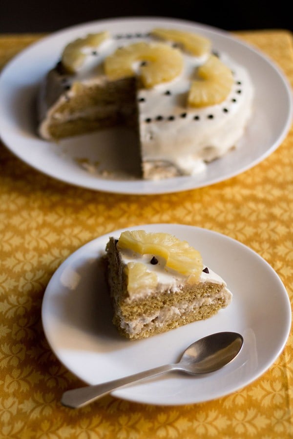 slice of pineapple pastry on white plate and pineapple cake in the background.