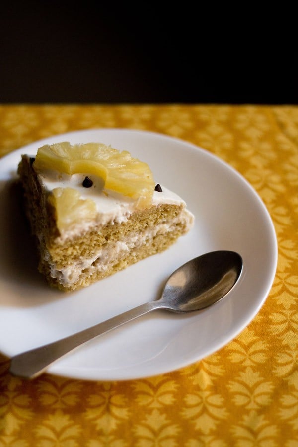 a slice of pineapple pastry on a white plate with spoon at side.