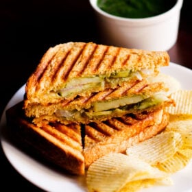 grilled sandwich with the filling side shown some potato wafers on a white plate