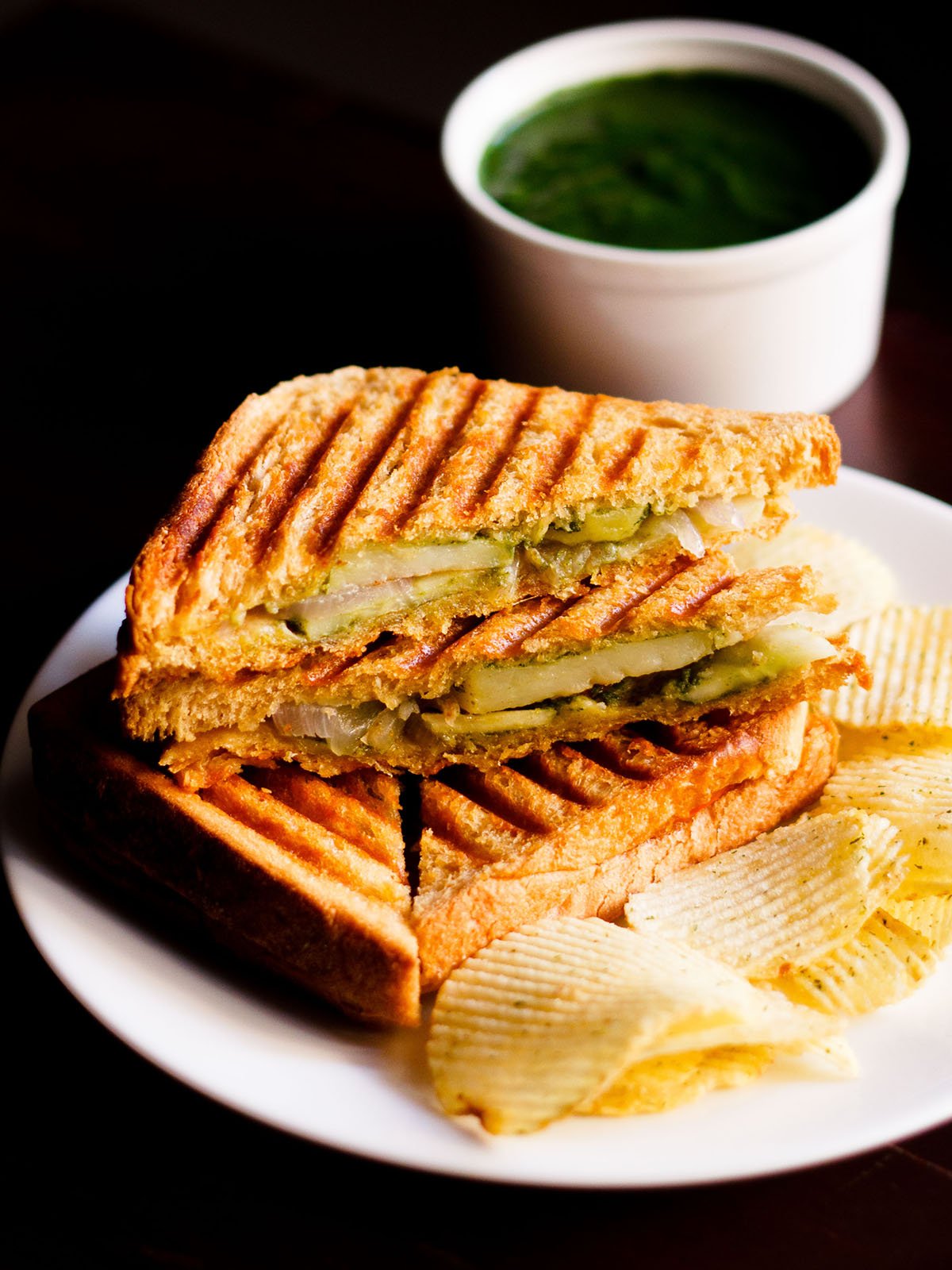 grilled sandwich with the filling side shown some potato wafers on a white plate