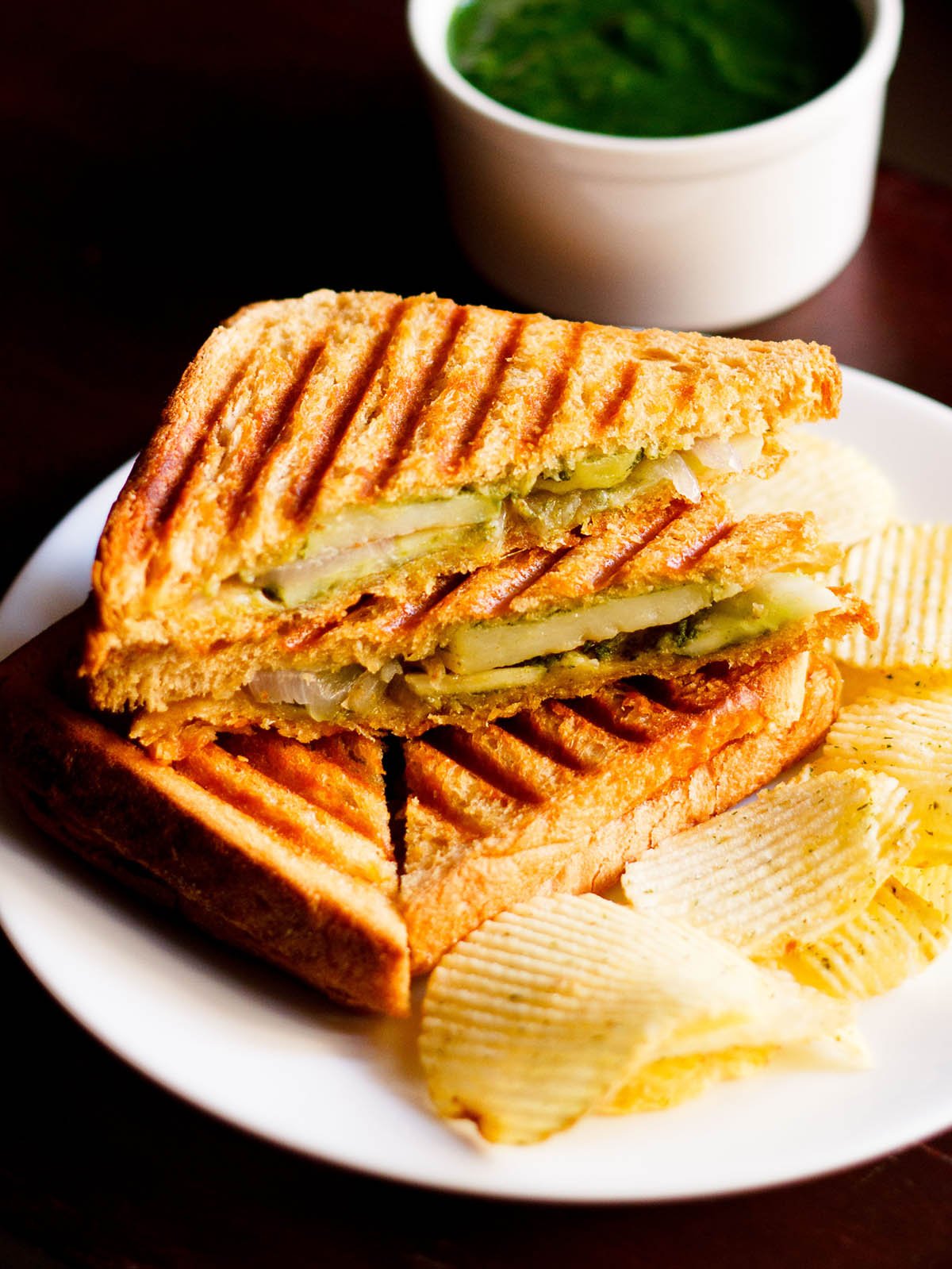 grilled sandwich with the filling side shown some potato wafers on a white plate