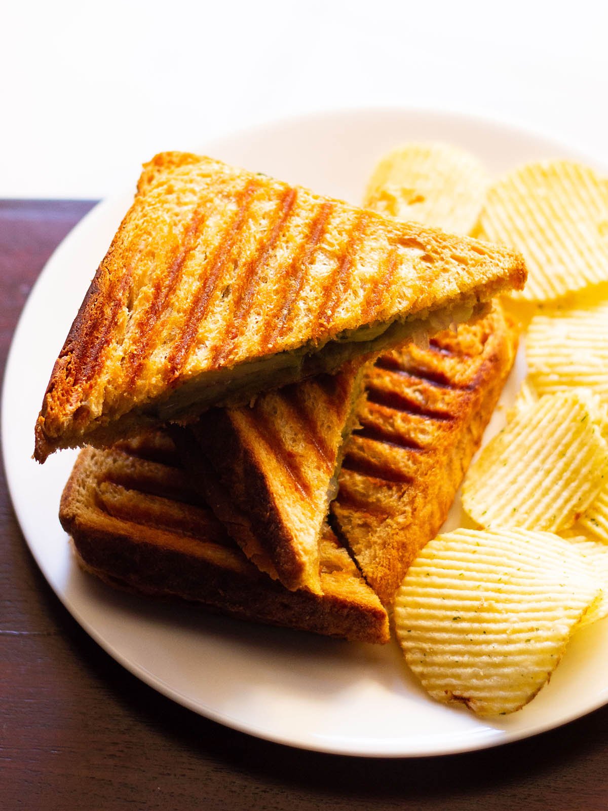 golden, crisp grilled sandwiches with a side of potato wafers on a white plate