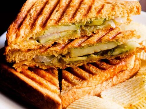 grilled sandwich with the filling side shown some potato wafers on a white plate