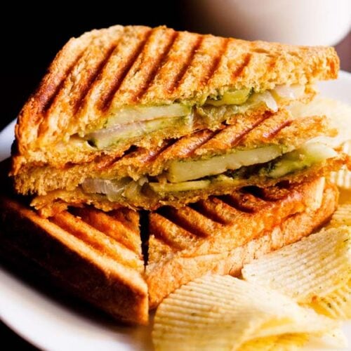 grilled sandwich with the filling side shown some potato wafers on a white plate
