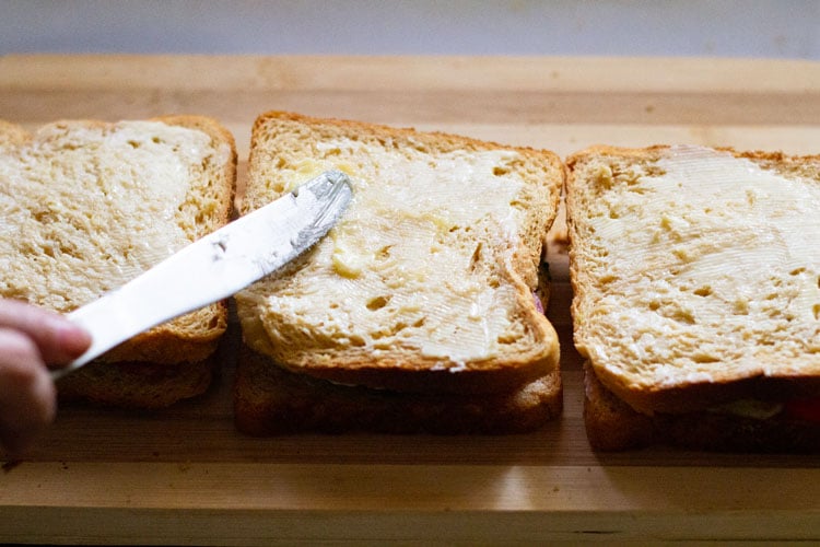 spreading butter on top side of assembled sandwich