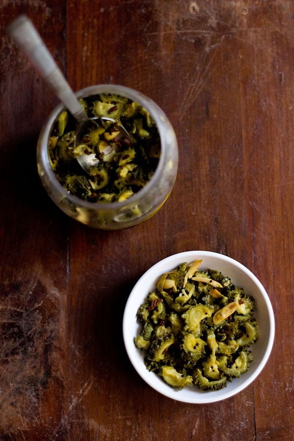 bitter gourd pickle or karela pickle served in a white bowl with a jar of pickle kept near it. 