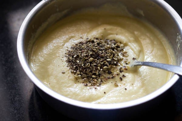 crushed whole black pepper and crushed coriander seeds added to prepared moong dal batter in bowl. 