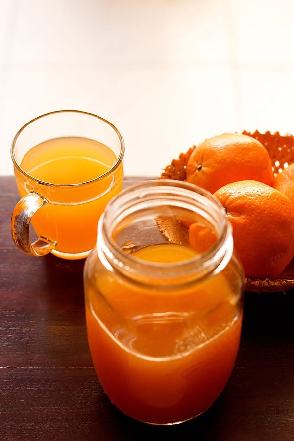 orange squash in a jar and orange drink in a glass and fresh oranges kept in the background. 