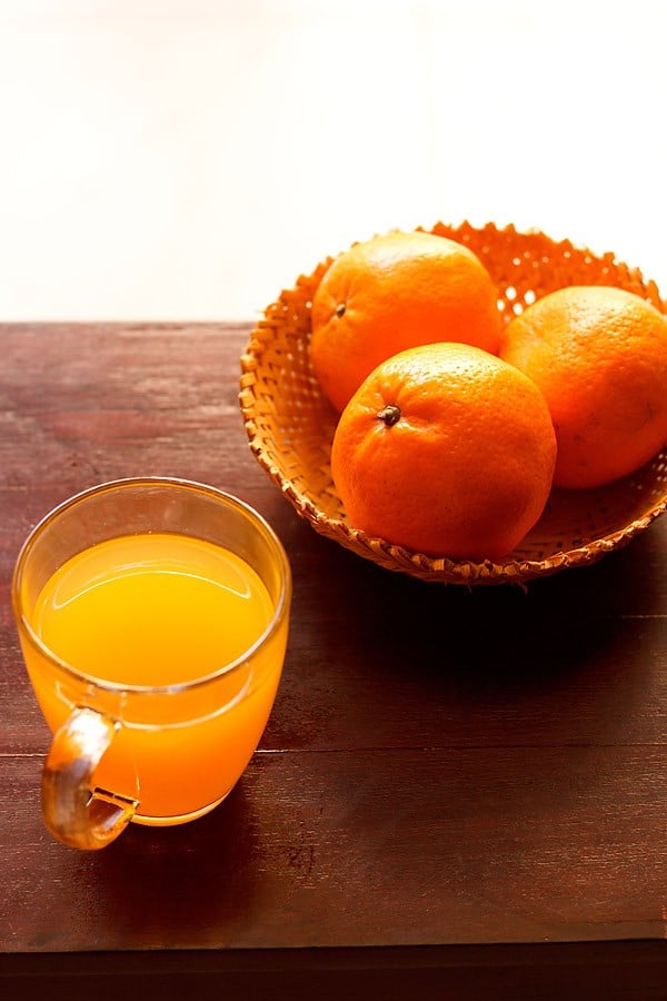 orange drink made from orange squash served in a glass and fresh oranges kept on the side. 
