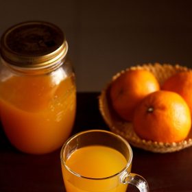 orange squash served in a glass with fresh oranges in a basket and squash in a jug kept at the back.