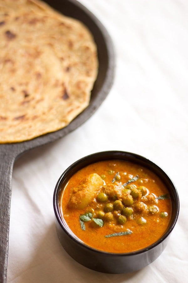potato peas kurma in a black bowl on a white tablecloth with a roti to the side.