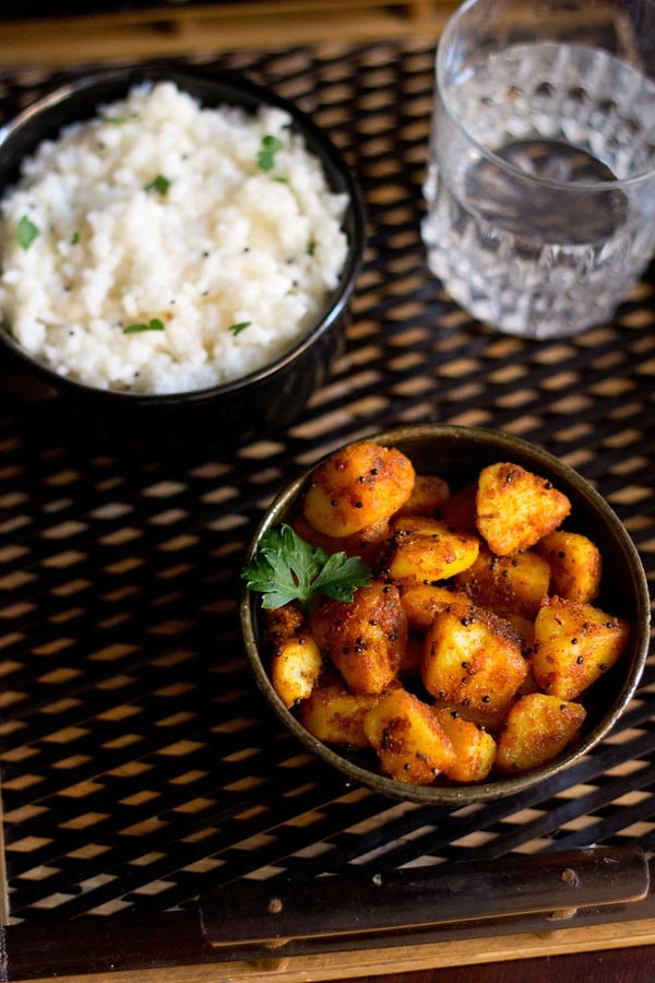 potato roast served in a bowl with a bowl of curd rice kept on the top left side and a glass of water kept on the top right side.