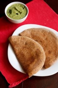 ragi dosa served on a white square plate on a red napkin with a side white bowl of green coconut chutney.