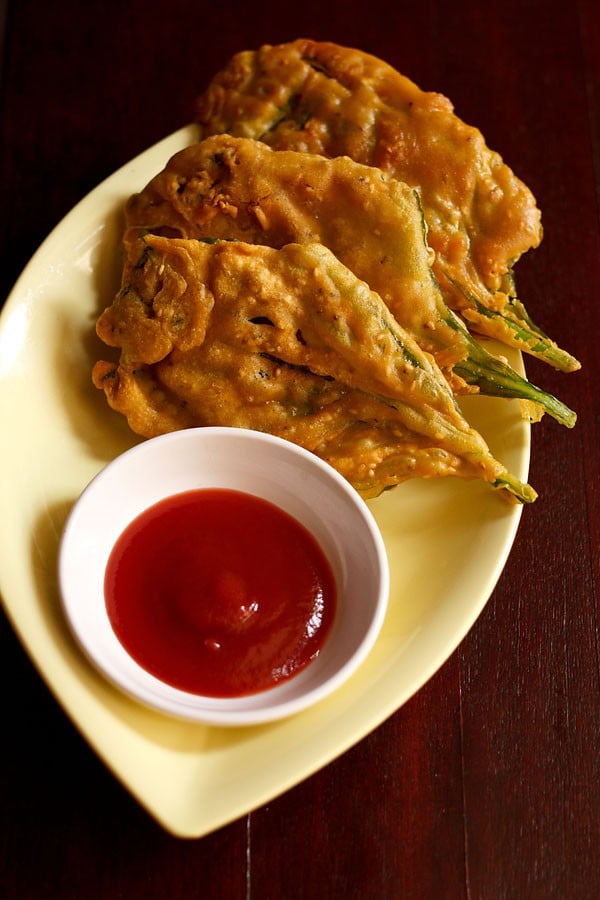 crispy spinach leaf fritters placed on a light yellow oval plate with ketchup in a small white bowl