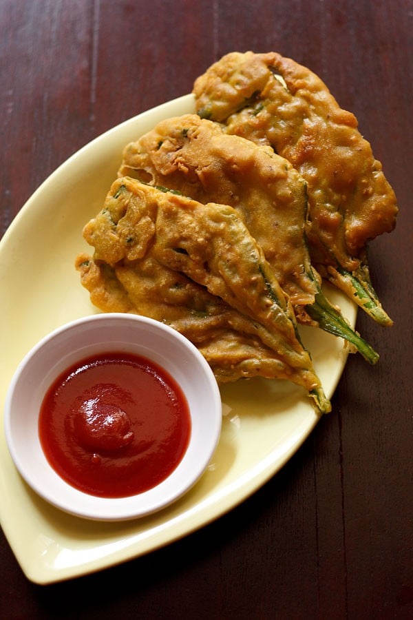 crispy spinach leaf fritters placed on a light yellow oval plate with ketchup in a small white bowl