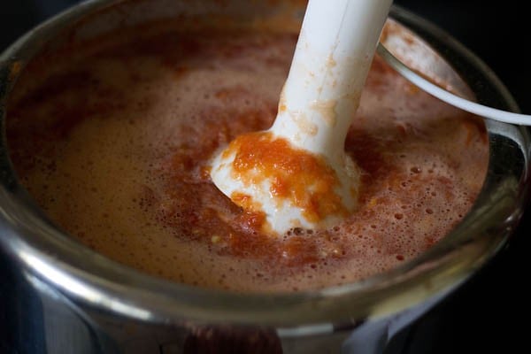 immersion blender blending softened tomatoes into a smooth puree