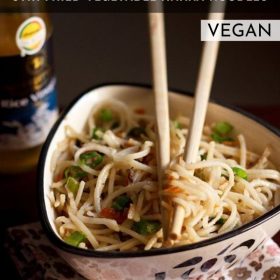 hakka noodles garnished with chopped spring onion greens and served in a triangular bowl on a printed napkin with cream colored bamboo chopsticks placed in it and text layover.