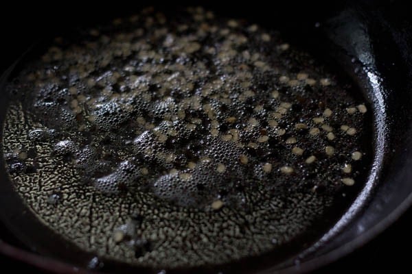 frying mustard seeds and urad dal in hot oil in a pan for aloo bonda recipe. 