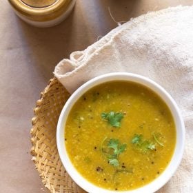 The amti is garnished with coriander leaves and served in a white bowl.