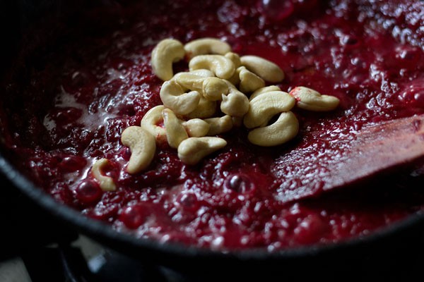 adding cashewnuts to grated beetroot and milk mixture in pan