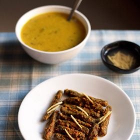 besan bhindi served on a white plate with a bowl of dal and a small bowl of ginger juliennes kept in the background.