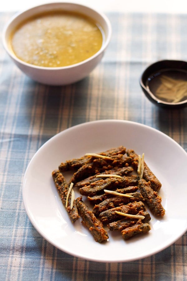 besan bhindi served on a white plate with a bowl of dal and a small bowl of ginger juliennes kept in the background. 