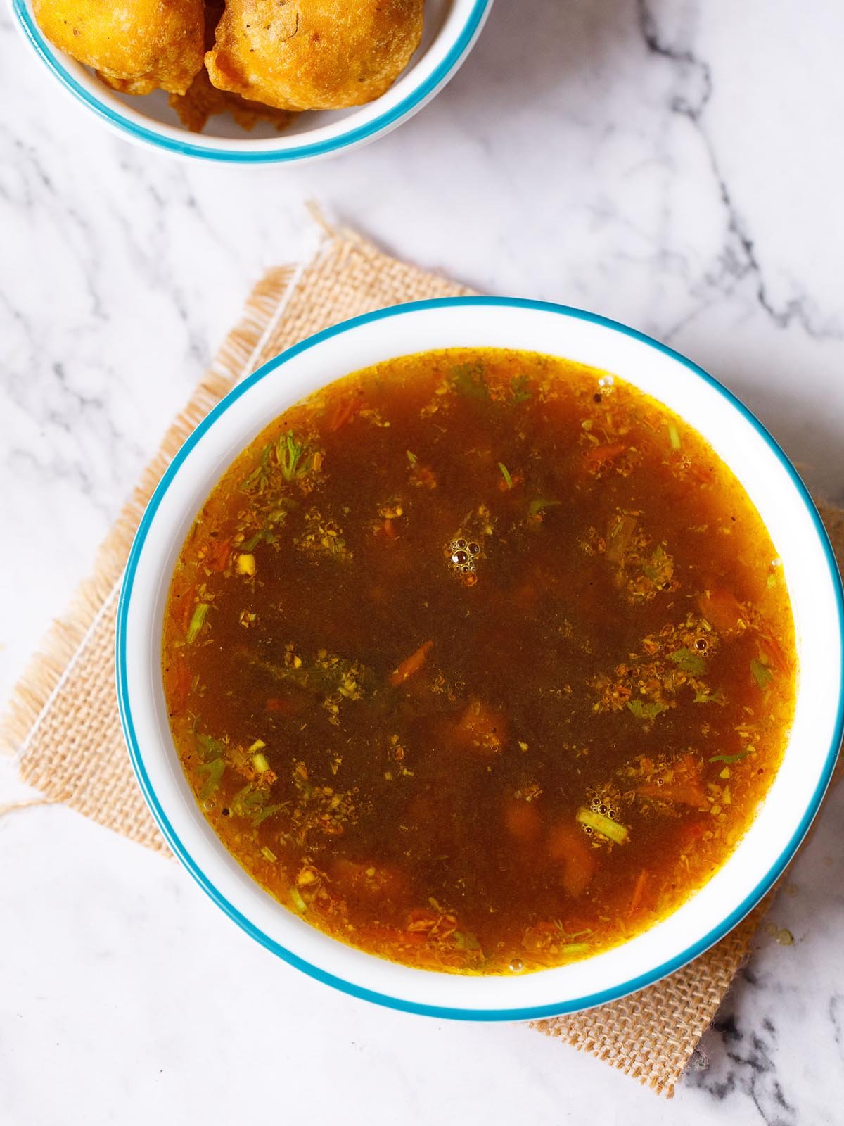 rasam served in a blue rimmed white bowl placed on a jute mat