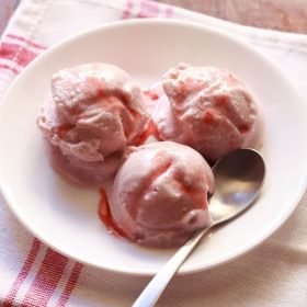 strawberry ice cream scoops served on a plate with fresh strawberry pieces.