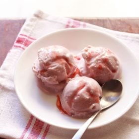strawberry ice cream scoops served on a plate with fresh strawberry pieces.