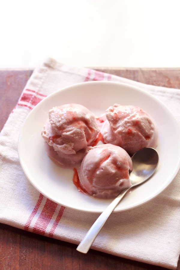 स्ट्राबेरी आइसक्रीम स्कूप्स को एक प्लेट में ताज़े स्ट्रॉबेरी के टुकड़ों के साथ परोसा जाता है।