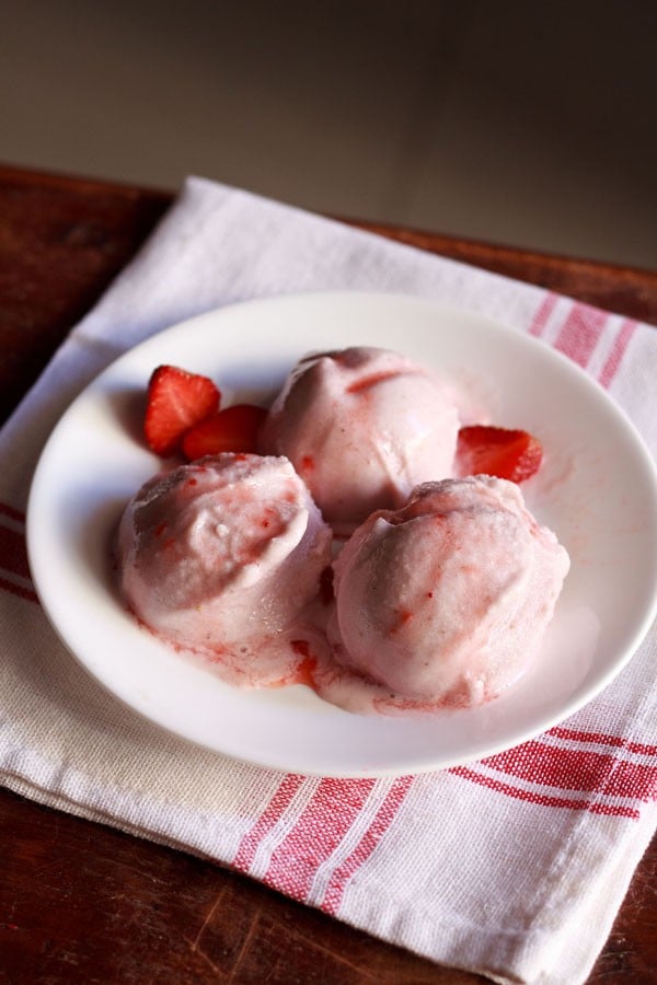 स्ट्राबेरी आइसक्रीम स्कूप्स को एक प्लेट में ताज़े स्ट्रॉबेरी के टुकड़ों के साथ परोसा जाता है 