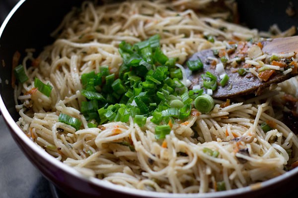 adding a garnish of spring onion greens on the stir-fried hakka noodles