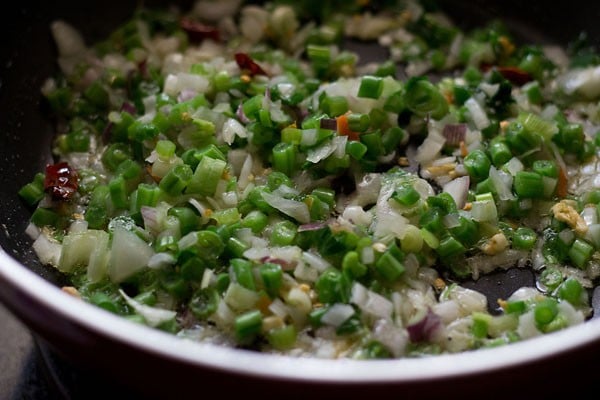 chopped spring onions (scallions) and finely chopped french beans being stir-fried in the pan