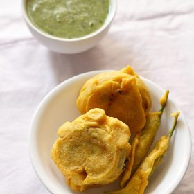 aloo bonda served on a white plate with a small bowl of green chutney kept on the top side.
