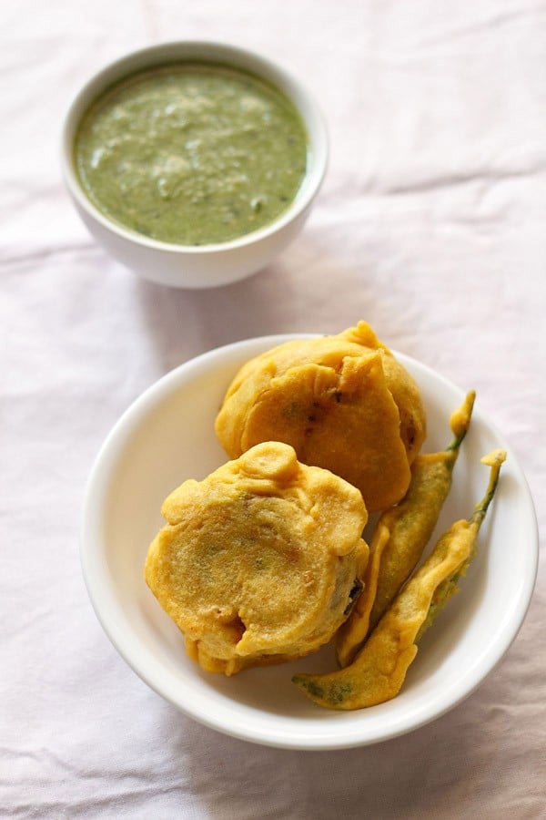 The aloo bonda was served on a white plate with a small bowl of green chutney on top.