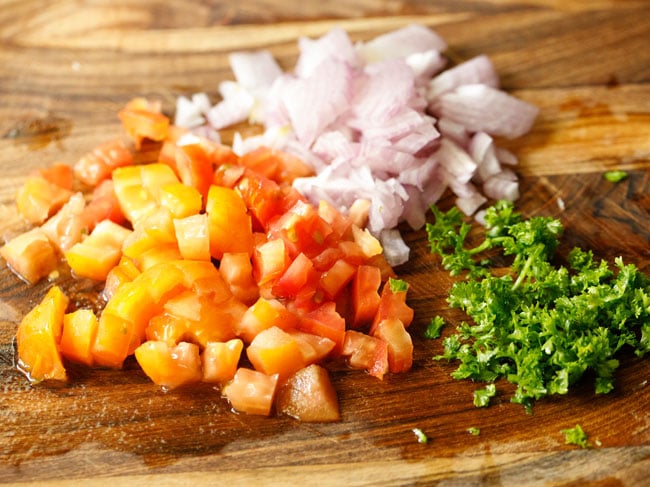 chopped onions, tomatoes and parsley on a cutting board.