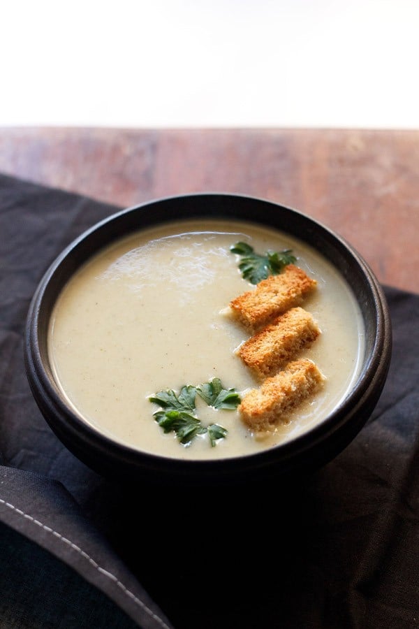 cream of celery soup in a black bowl garnished with 3 croutons and some fresh parsley leaves.