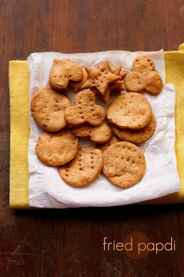 papdi placed on a kitchen paper tissue kept on a yellow colored kitchen napkin on a wooden surface with text layover.