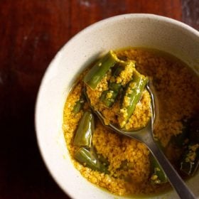 green chilli pickle in a spoon in a bowl filled with chilli pickle.