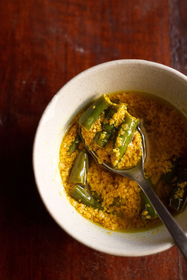 green chilli pickle in a spoon in a bowl filled with chilli pickle.