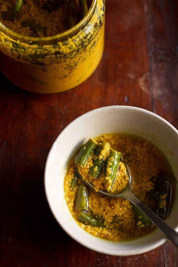 portion of green chilli pickle over spoon on top of bowl with the chilli pickle.