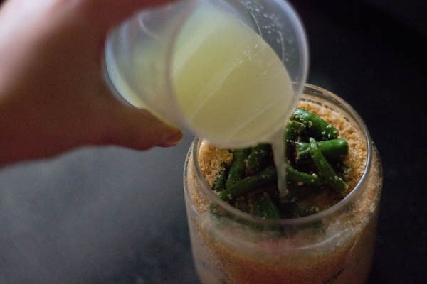 lemon juice poured into green chilli pickle inside the jar.