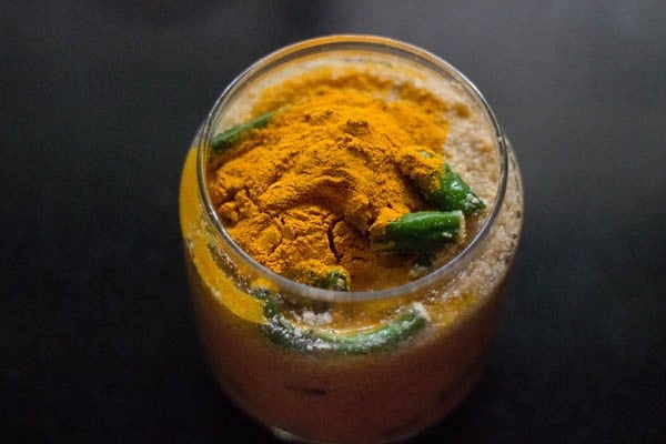 turmeric powder on top of green pickle mixture in glass jar.